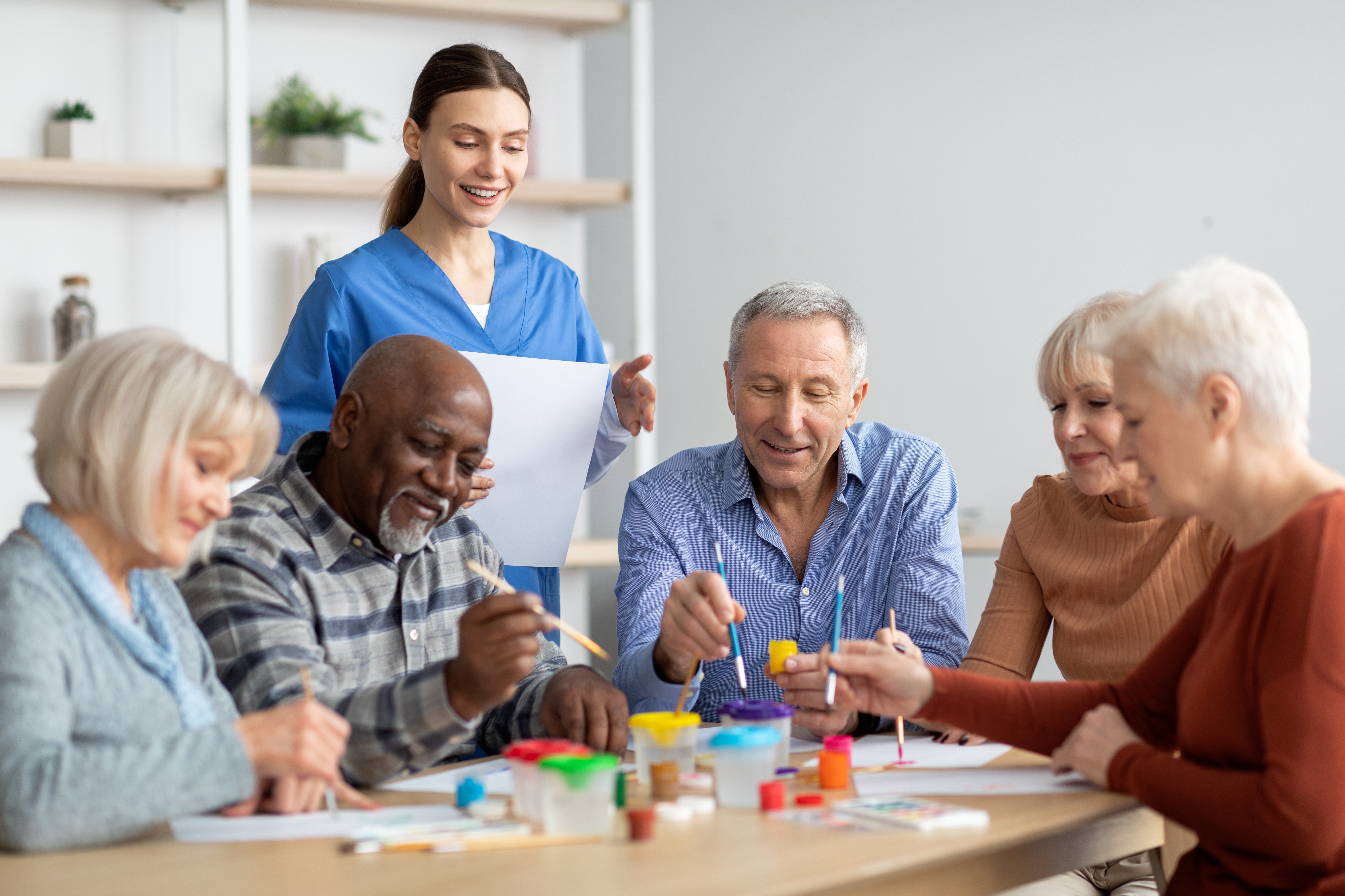 multiracial elder group painting together with nurse overseeing